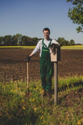 Jakob steht mit einem Spaten neben einer Insekten-Nisthilfe 